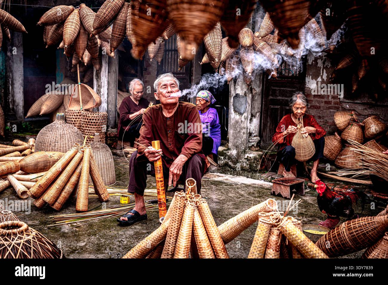 L'uomo realizza trappole per pesci di bambù mentre fuma in laboratorio con altri artigiani ad Hanoi, Vietnam Foto Stock