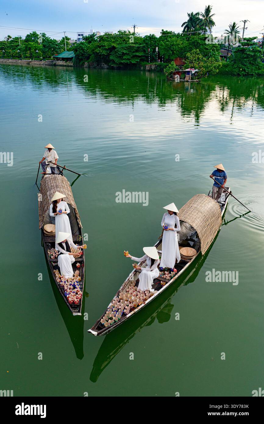 Le donne in abito tradizionale galleggiano lanterne sul fiume durante una celebrazione serale nel Vietnam centrale Foto Stock