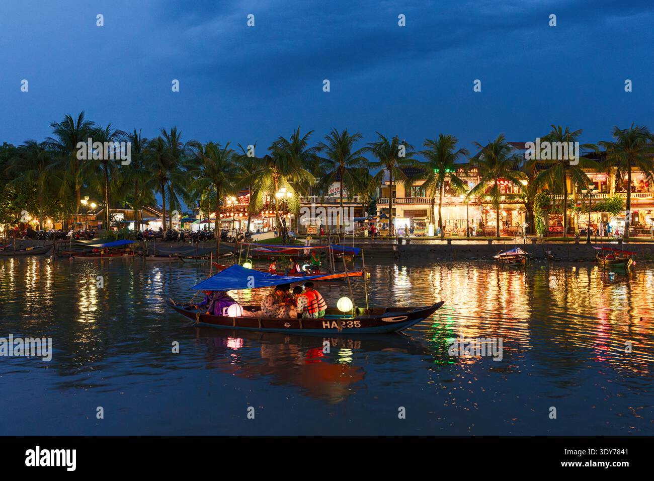 Le barche turistiche navigano sul fiume Thu Bon al crepuscolo con luci e palme a Hoi An, provincia di Quang Nam, Vietnam Foto Stock