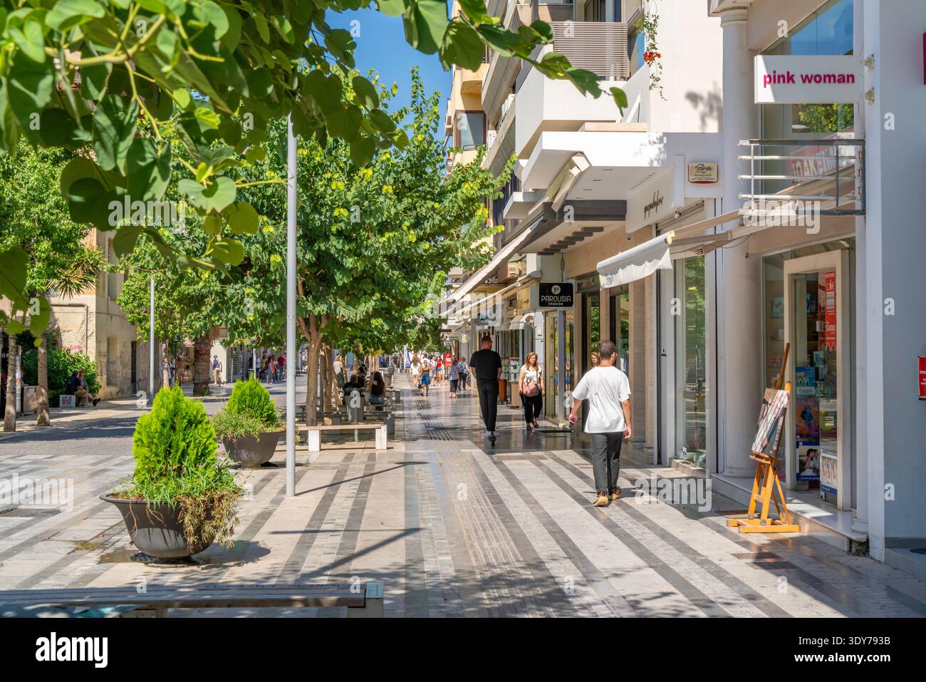 Negozi e persone riempiono le strade animate in una luminosa giornata di sole nel cuore di una città di Creta, in Grecia Foto Stock