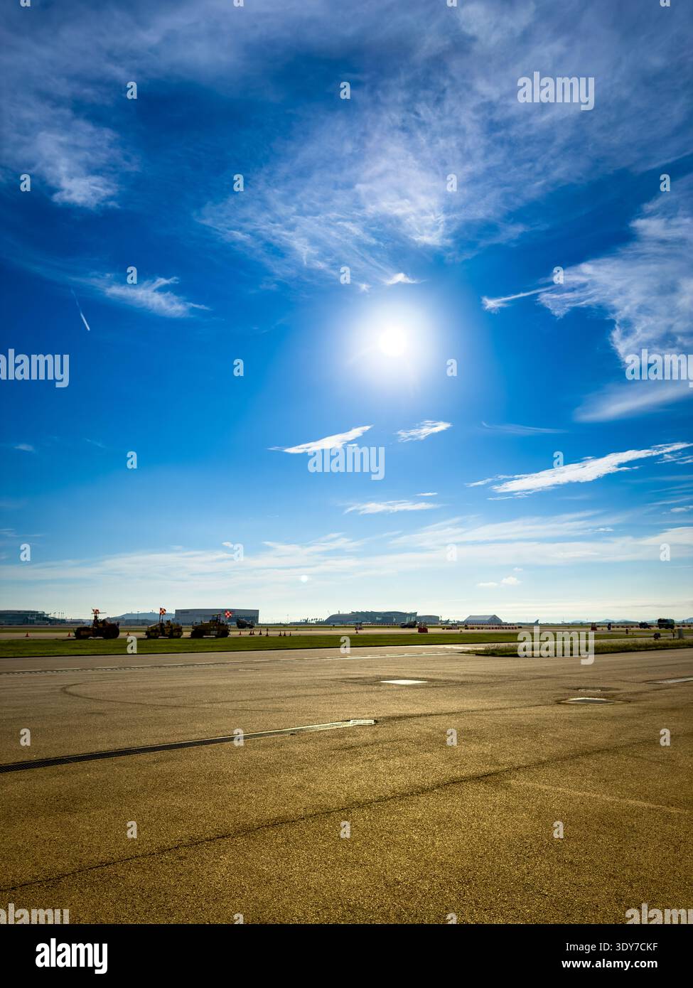 Pista aeroportuale e pista di rullaggio sotto il sole luminoso e il cielo blu con veicoli di servizio a terra, ampi spazi aperti e background aeronautico. - Immagine stock catturata con smartphone