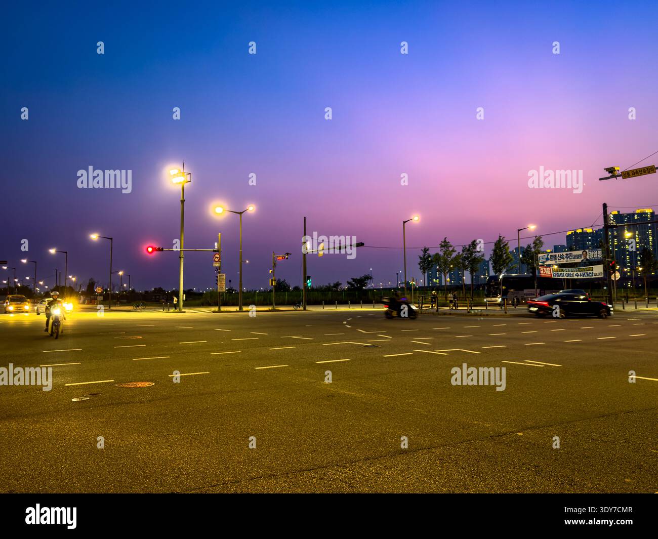 Incrocio della città al crepuscolo con semafori, veicoli in movimento e colorato cielo crepuscolare, scena urbana serale di strada. Foto Stock