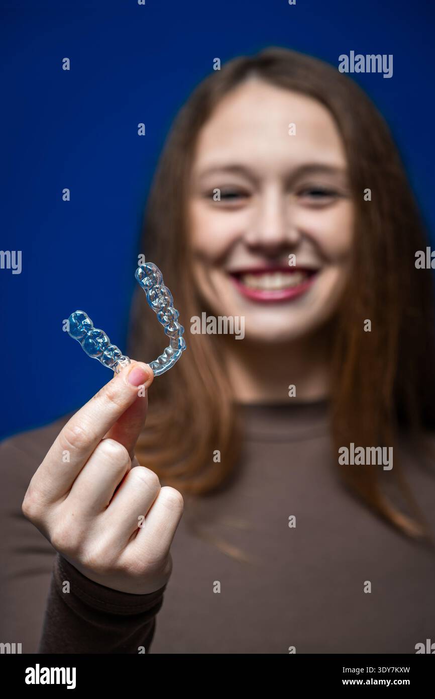 Giovane donna che tiene in mano un allineatore dentale chiaro, sorridente e che promuove l'ortodonzia moderna e le soluzioni di correzione dei denti Foto Stock