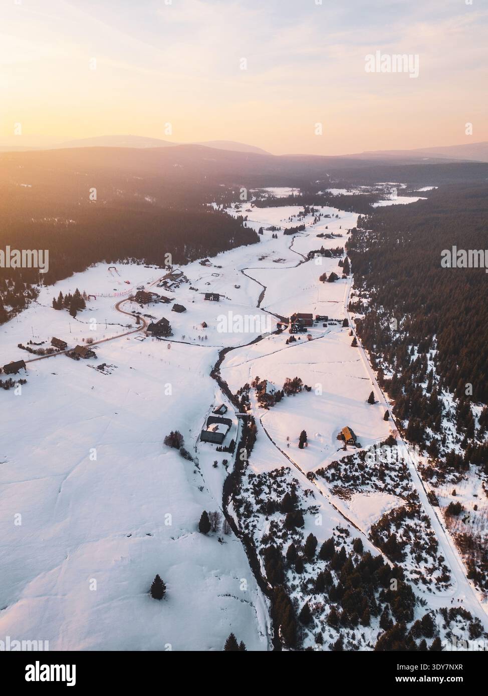 Il villaggio di montagna di Jizerka mostra un paesaggio innevato dall'alto. Le case sono circondate da campi bianchi e alberi. La luce del sole crea ombre morbide in tutta la terra d'inverno. Foto Stock