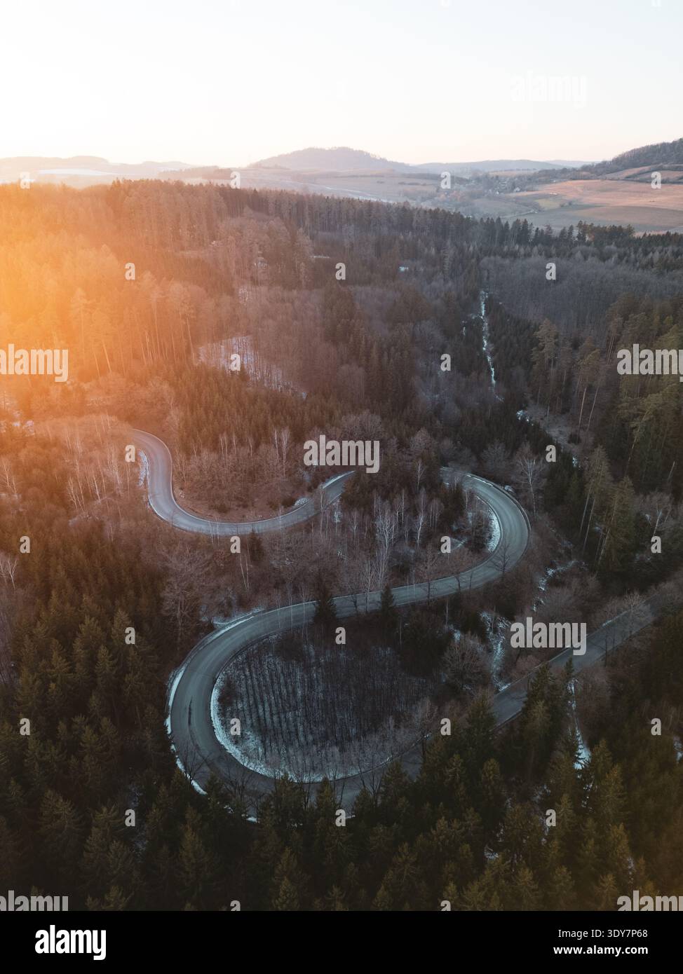 Una strada tortuosa serpeggia attraverso una lussureggiante foresta mentre il sole tramonta, proiettando un caldo bagliore sul paesaggio. Gli alberi lungo il percorso, arricchendo le bellezze naturali della zona. Foto Stock