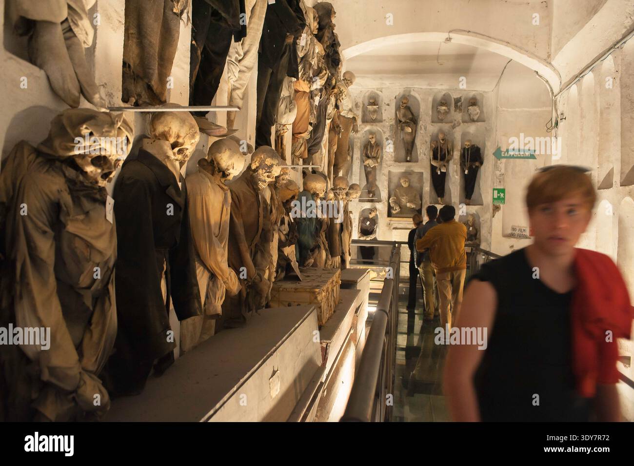 Catacombe di Palermo, vista di un turista che cammina davanti a una fila di scheletri situati all'interno delle Catacombe dei Cappuccini, Palermo, Sicilia. Foto Stock