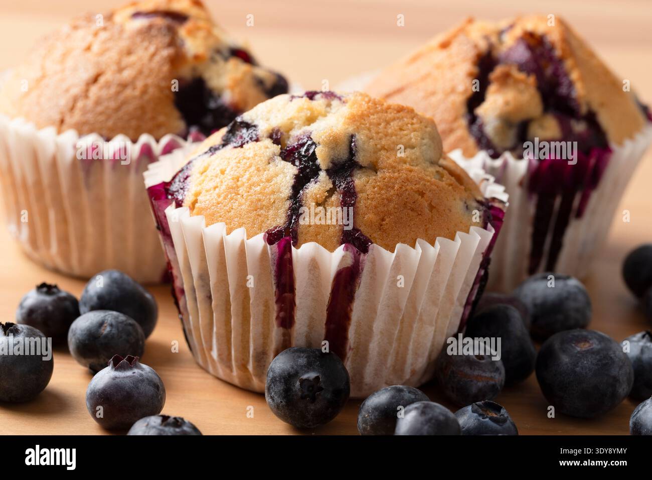 Primo piano: Muffin ai mirtilli fatti in casa con il succo di mirtillo che gocciola nei contenitori di carta Foto Stock