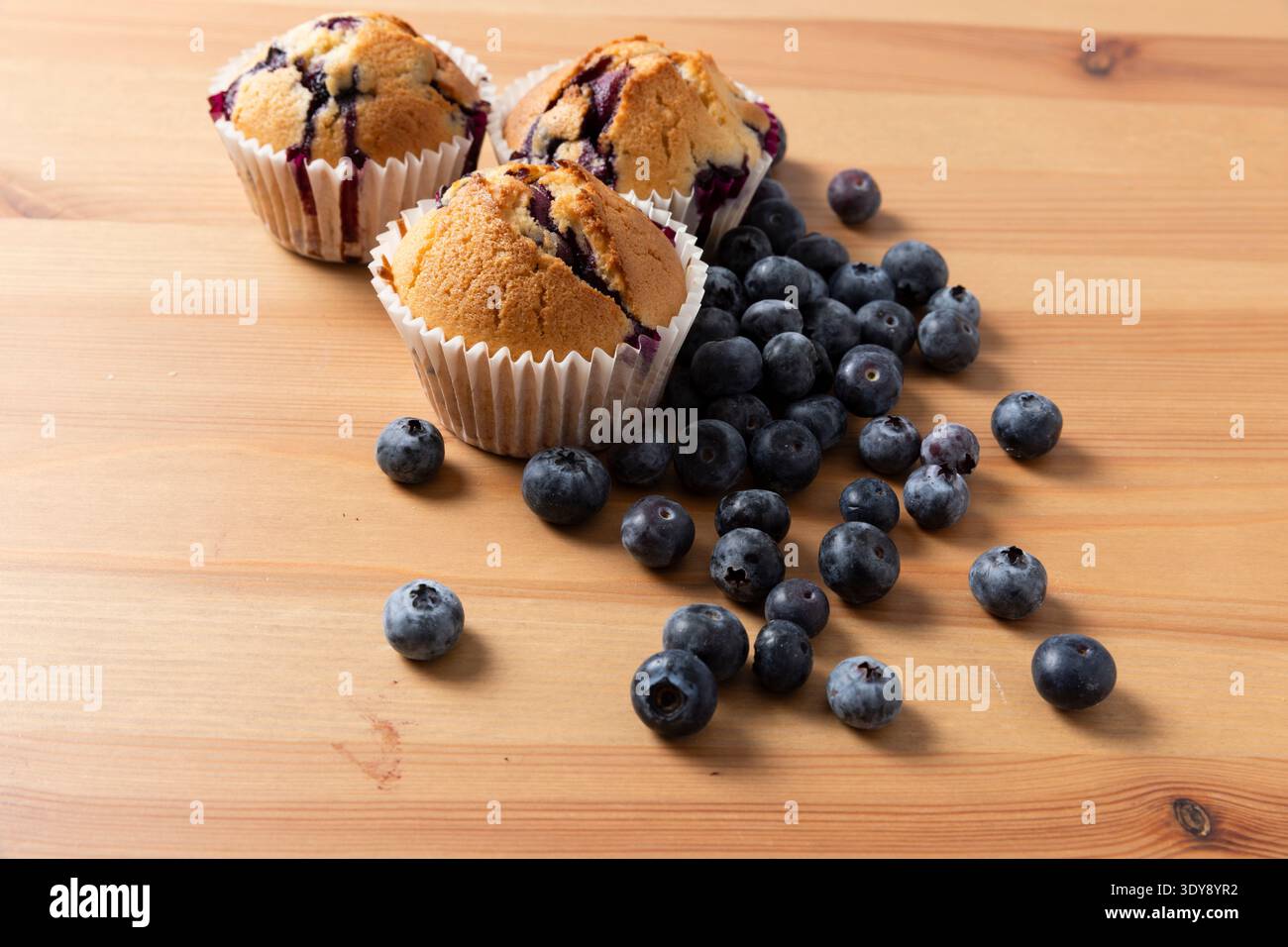 Tre muffin ai mirtilli fatti in casa con mirtilli freschi sparsi su un tavolo di legno, orizzontale Foto Stock