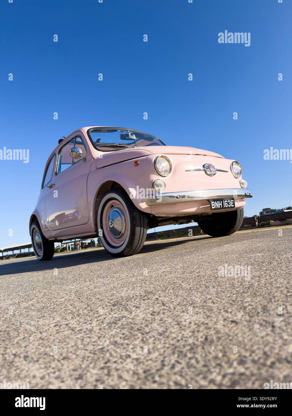 Vista grandangolare bassa di una classica Fiat 500 vintage degli anni '60 rosa pallido parcheggiata su pavimentazione in asfalto vicino al bordo del porto a North Shields Fish Quay, UK - Immagine stock catturata con smartphone