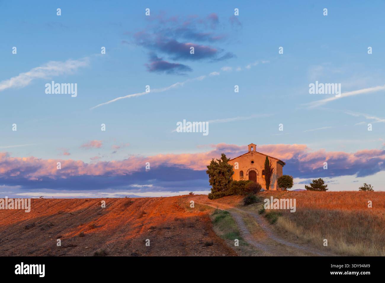 Piccola cappella in piedi su una collina illuminata dalla luce della sera, con un cielo colorato Foto Stock