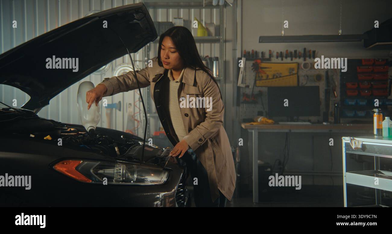 In un'officina domestica in stile industriale, illuminata e luminosa, Woman esegue la manutenzione essenziale del veicolo dopo il tragitto. Moderno spazio garage con strumenti di diagnostica digitale e hardware organizzato a portata di mano. Foto Stock