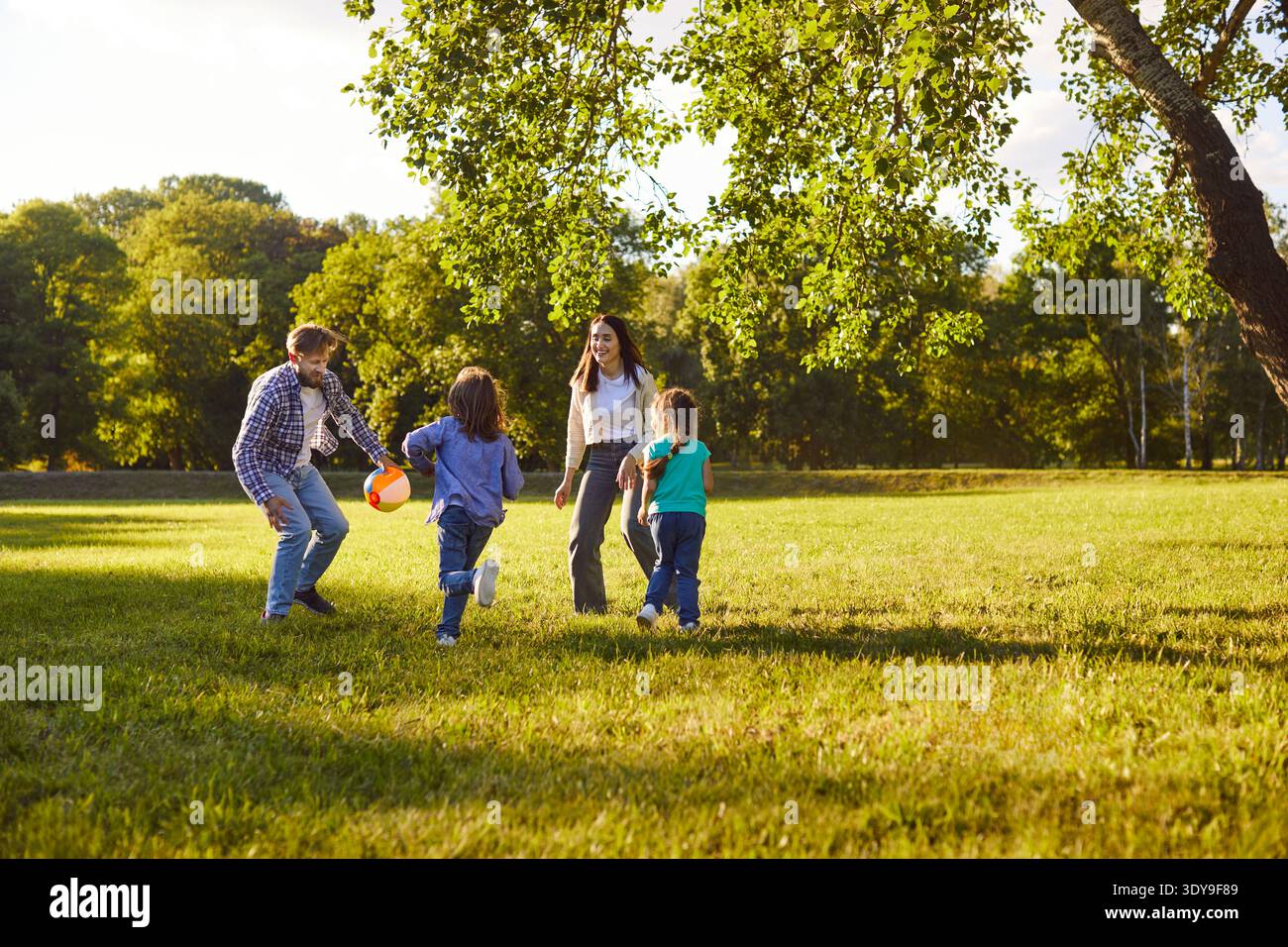 I bambini attivi e i loro genitori giocano a calcio nel parco, si muovono e ridono Foto Stock