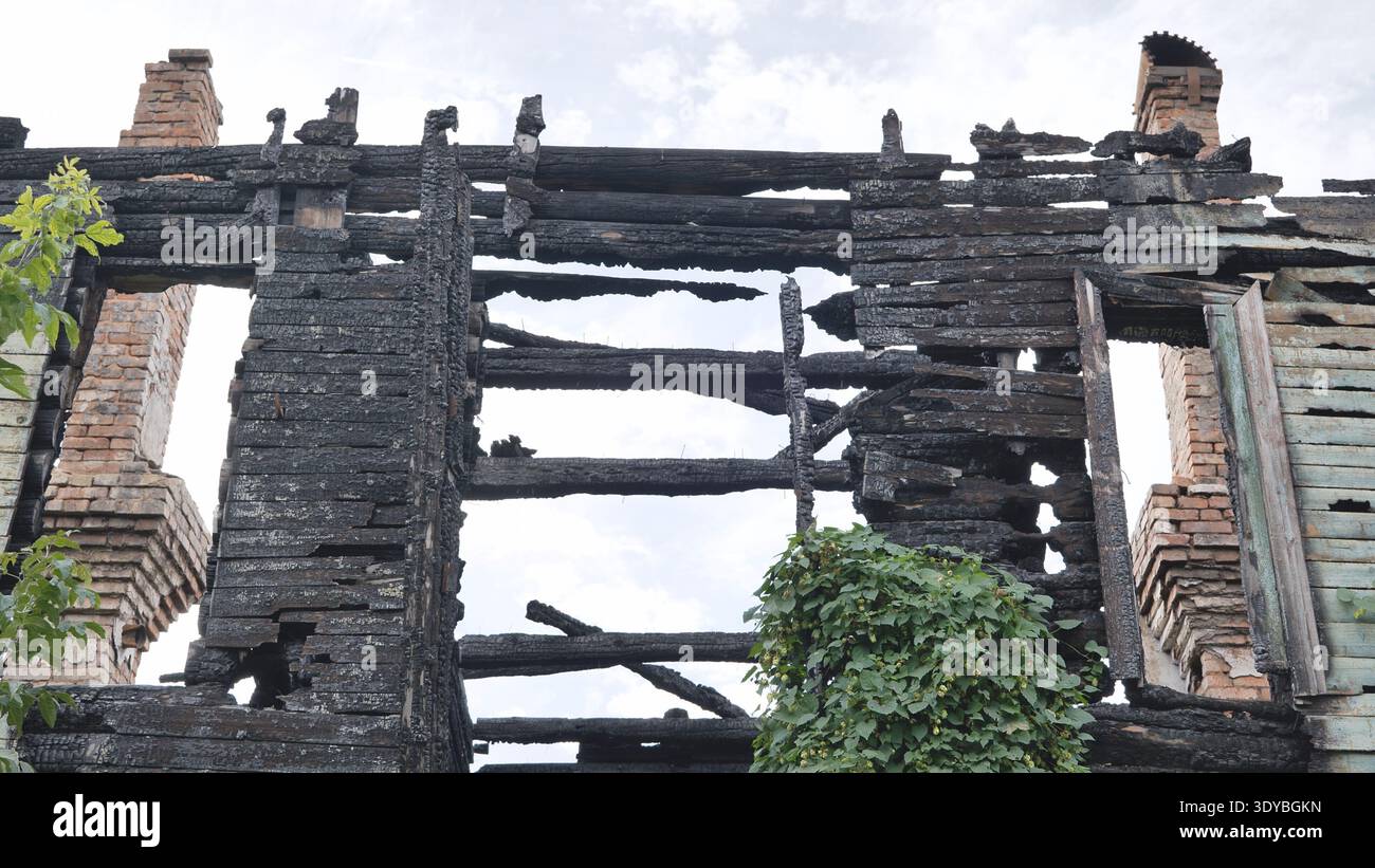 Resti carbonizzati di una casa di legno bruciata con camini in mattoni contro un cielo nuvoloso Foto Stock