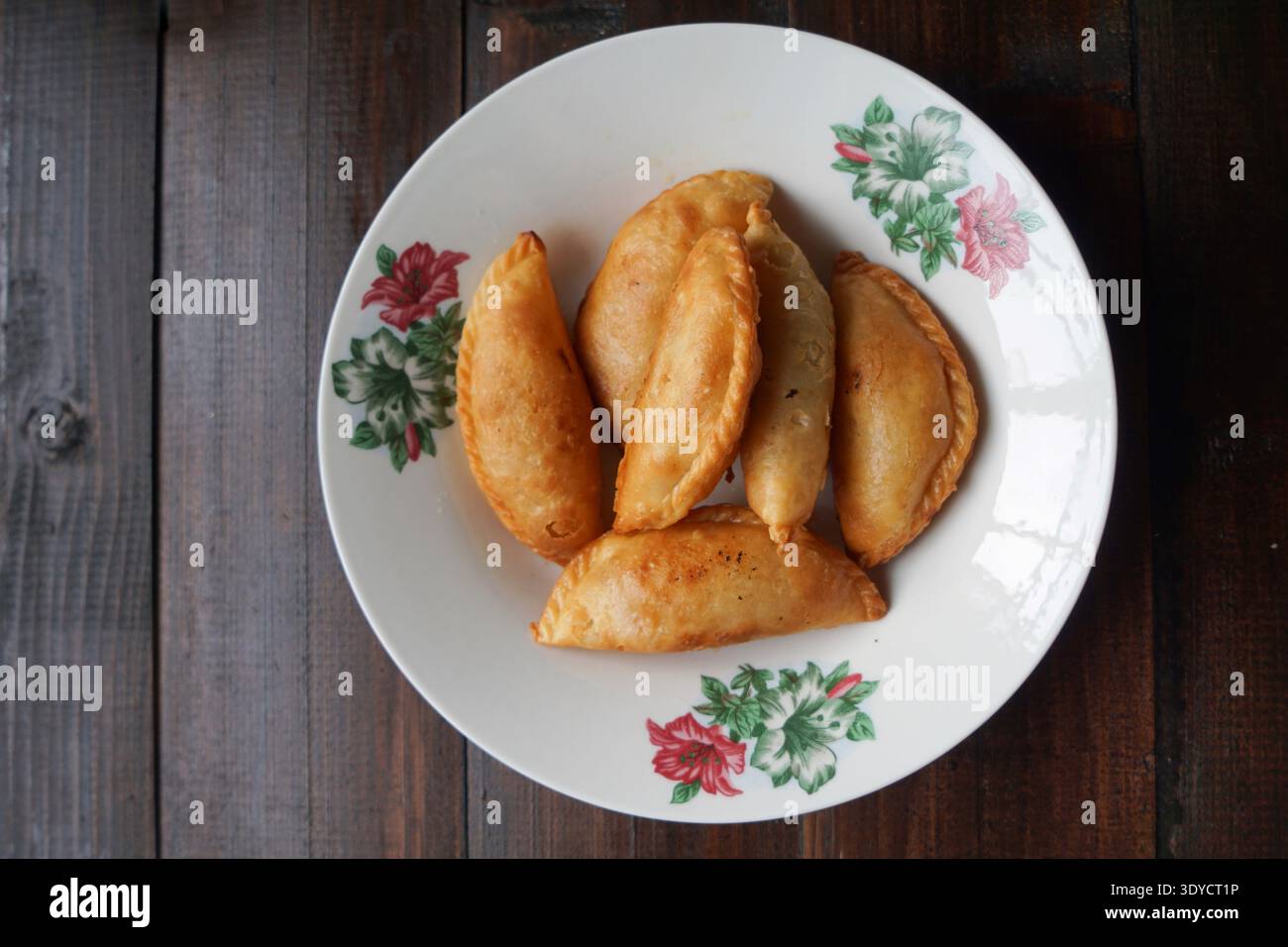 Sei spugne di curry dorate disposte su un piatto floreale su sfondo di legno scuro. Foto Stock