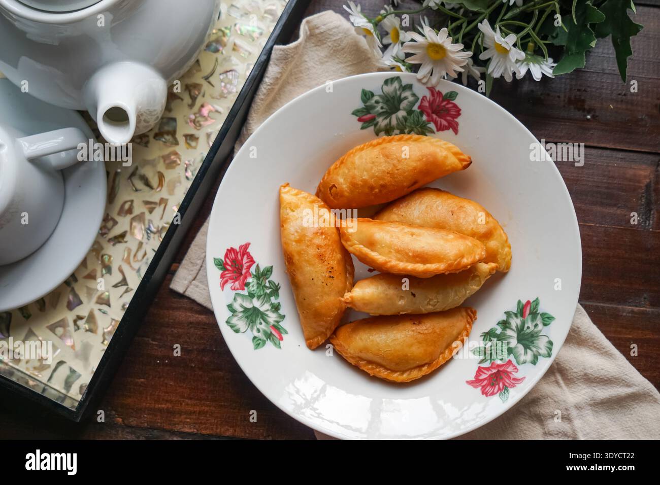 Sei spugne di curry dorate disposte su un piatto floreale su sfondo di legno scuro. Foto Stock