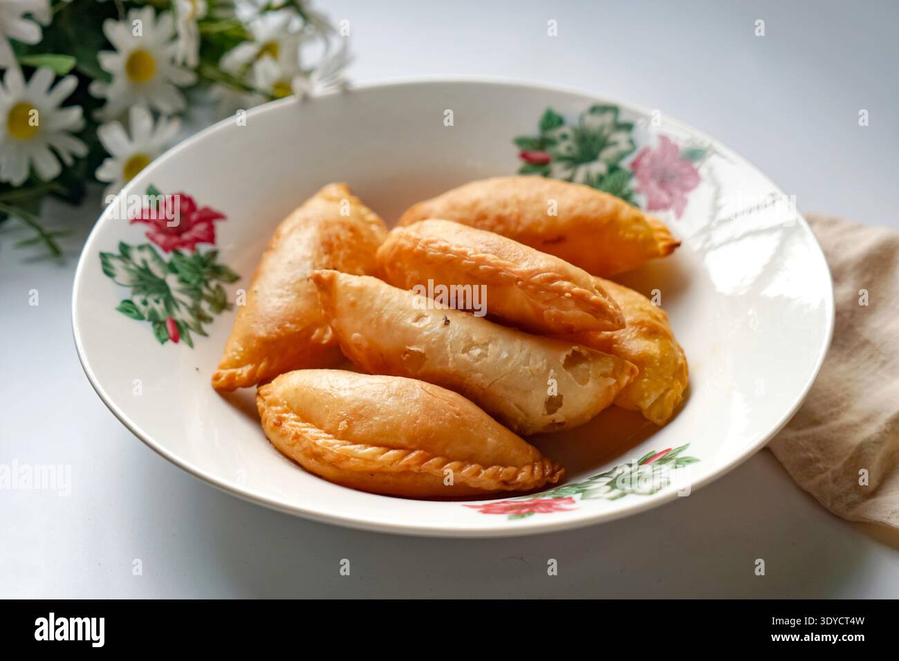 Un piatto di spugne di curry dorate con set da tè e margherite su sfondo bianco. Foto Stock