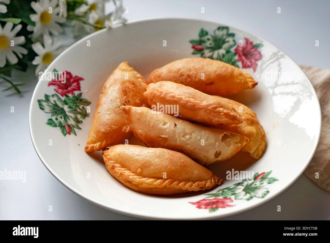 Un piatto di spugne di curry dorate con set da tè e margherite su sfondo bianco. Foto Stock