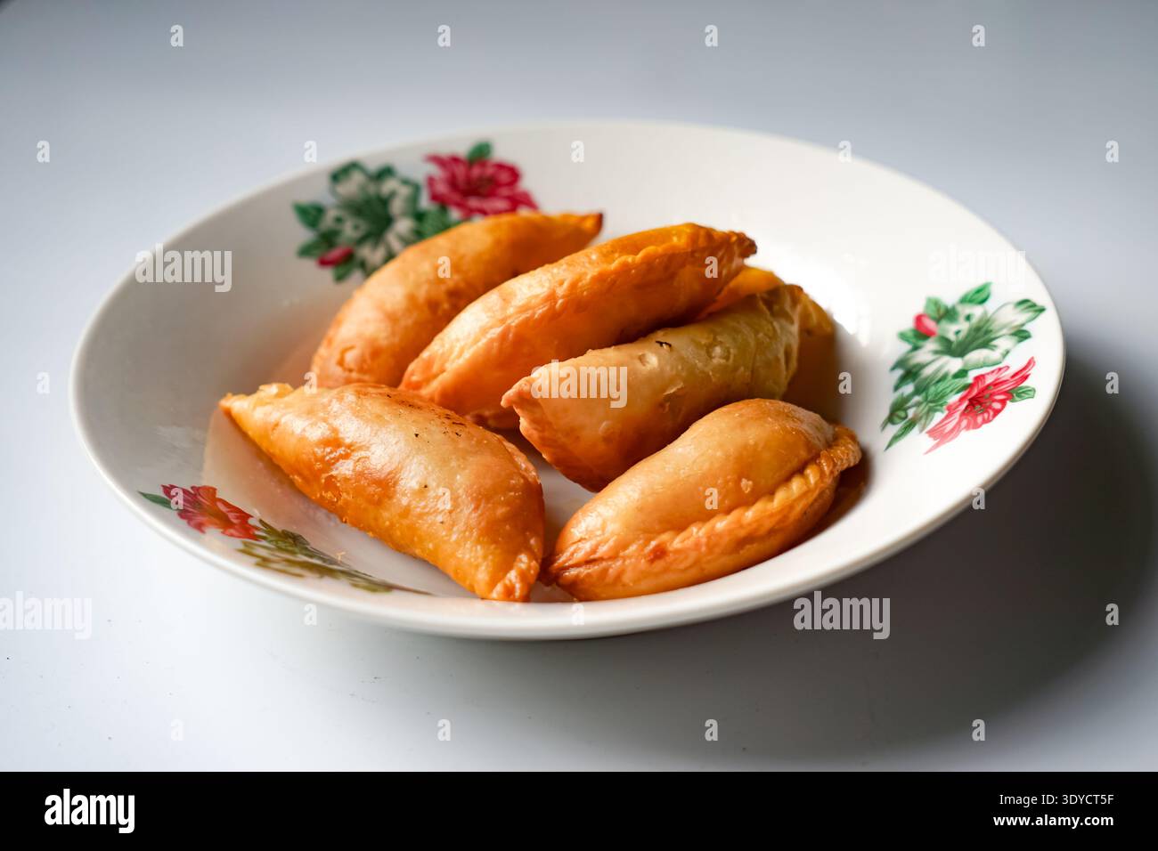 Un piatto di spugne di curry dorate con set da tè e margherite su sfondo bianco. Foto Stock
