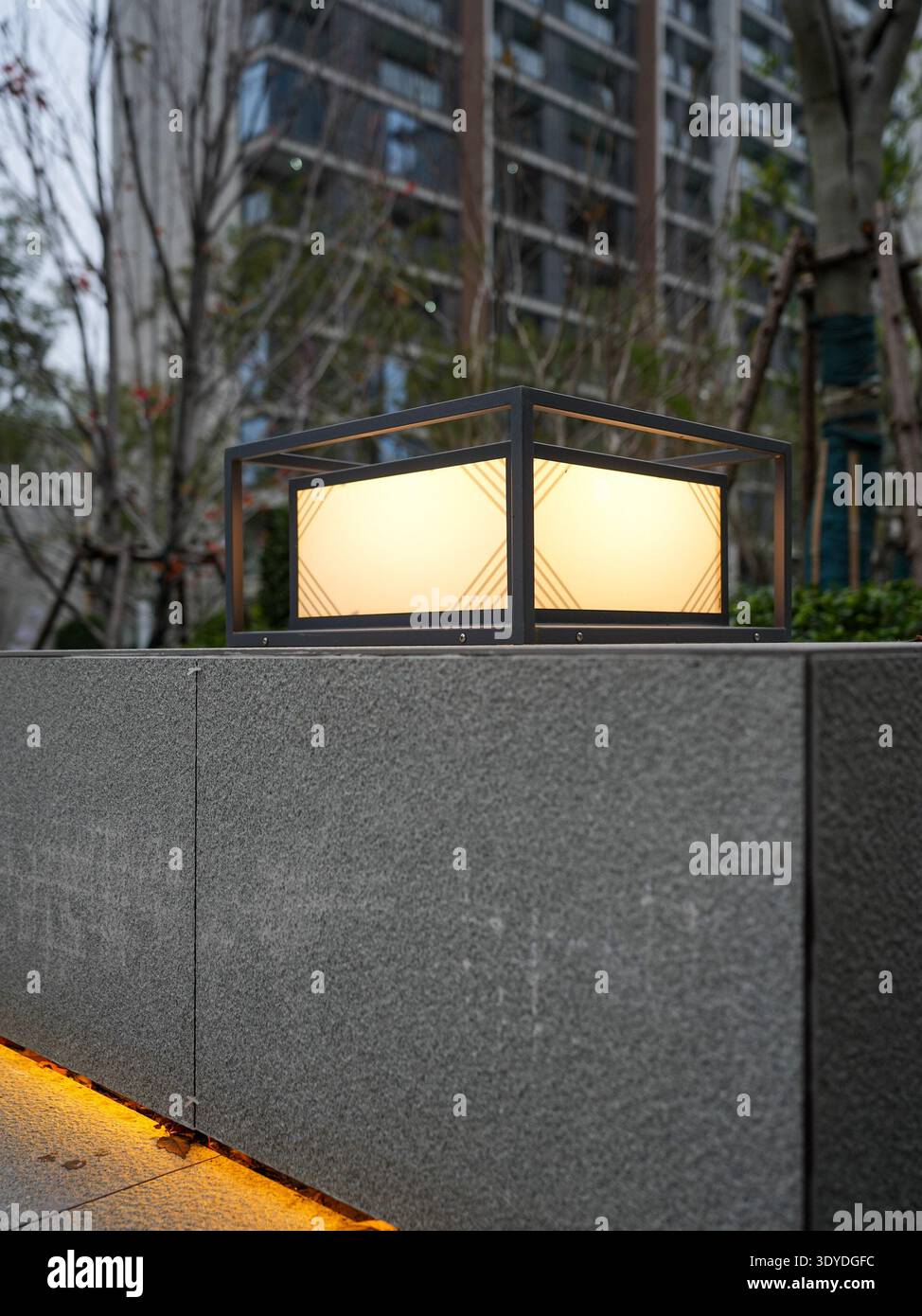 Vista dettagliata di una moderna lampada quadrata luminosa per esterni e di una calda illuminazione a strisce nascoste su un muro in pietra. L'immagine trasmette un design elegante e un design elegante Foto Stock