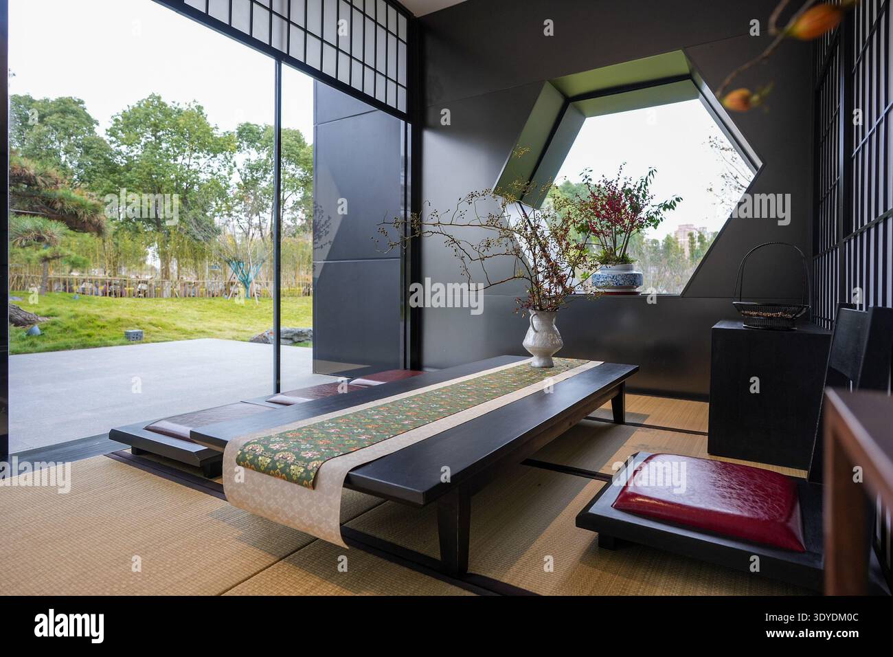 Vista dal pavimento tatami di una sala da tè Zen che guarda oltre un basso tavolo verso un lussureggiante giardino verde attraverso grandi finestre aperte. L'immagine trasmette il marinaio Foto Stock