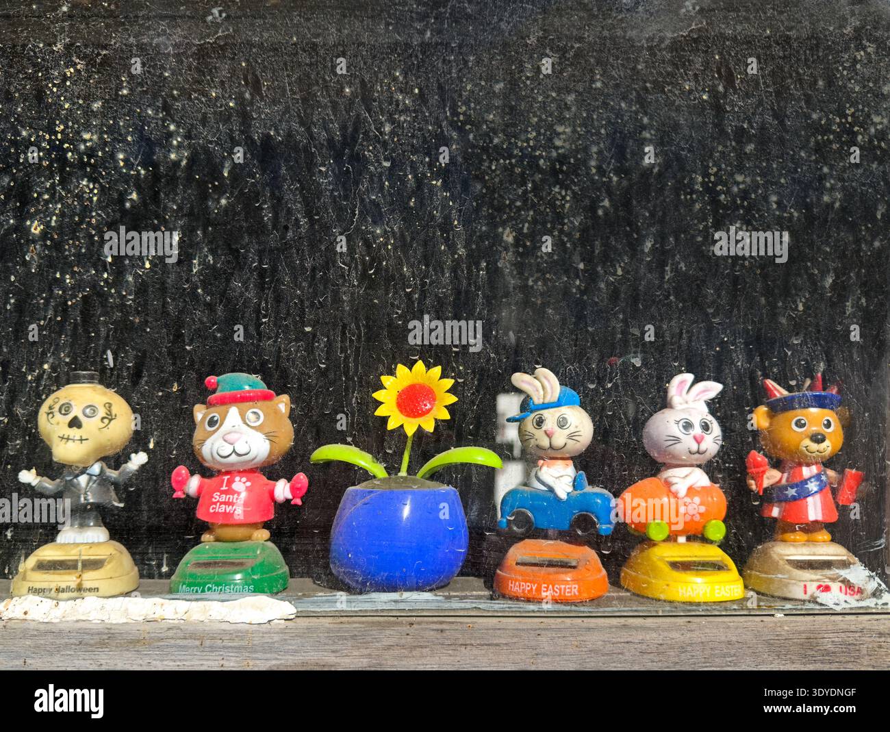 Una fila di sei giocattoli a forma di bobblehead fiancheggiano il davanzale di una vecchia e sporca finestra. Foto Stock