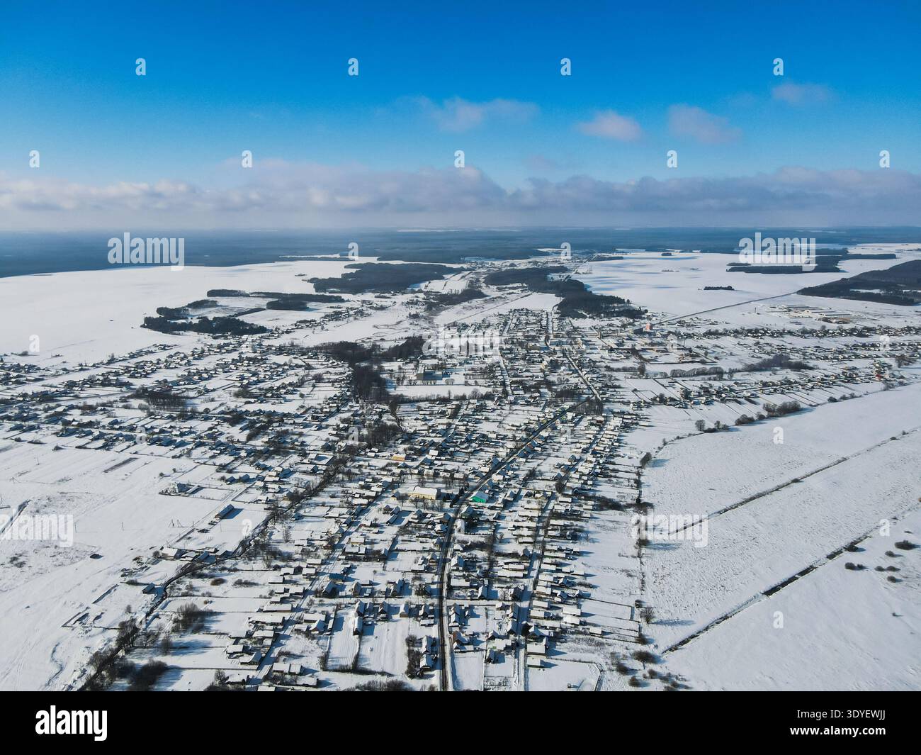 Scena aerea di mezzogiorno di una piccola città bielorussa nella neve profonda. Le strade a griglia e le case basse si estendono su una pianura, incorniciata da cinture di alberi scuri e campi, con una gent Foto Stock