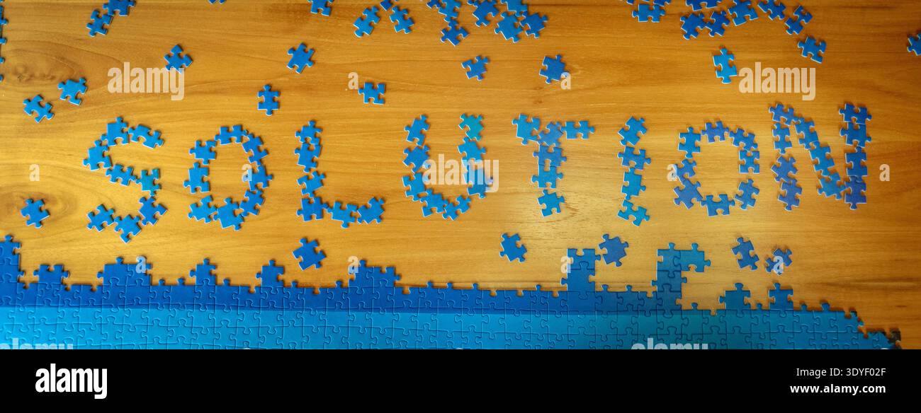 Concetto di soluzione scritto con pezzi di puzzle blu su un tavolo di legno con pezzi sparsi intorno. Rappresentazione creativa della risoluzione dei problemi, della strategia. Foto Stock