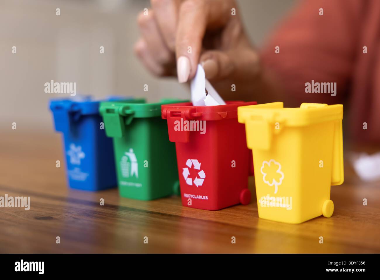 Posizionare manualmente un piccolo pezzo di carta in un contenitore di riciclaggio miniaturizzato Foto Stock
