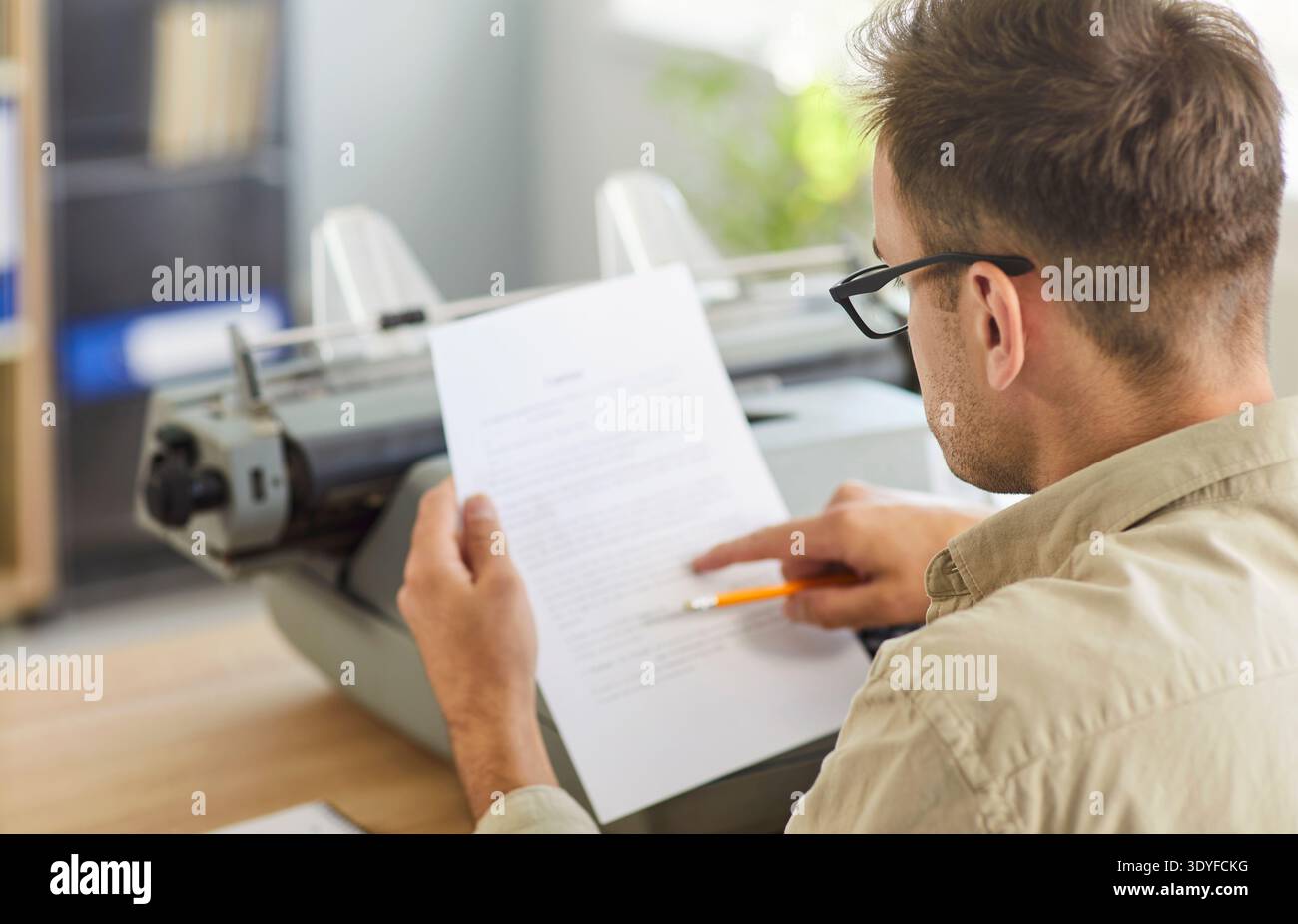 Primo piano di un uomo che ripara la pagina con una matita accanto alla macchina da scrivere vintage in ufficio Foto Stock