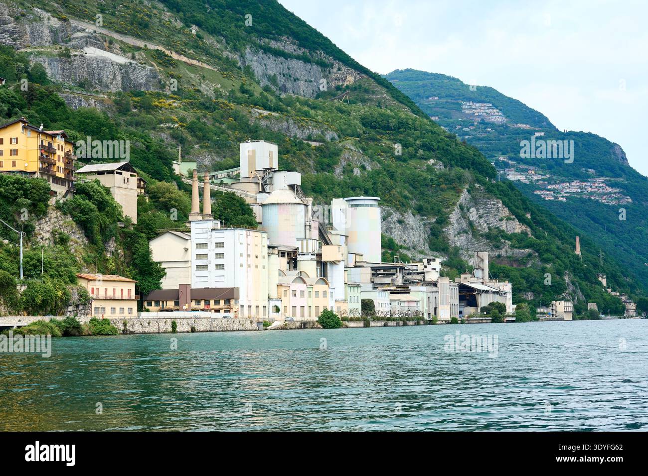 Edifici industriali, silos e camini situati direttamente accanto al lago, circondati da ripide colline. Gestito da Heidelberg Materials Foto Stock
