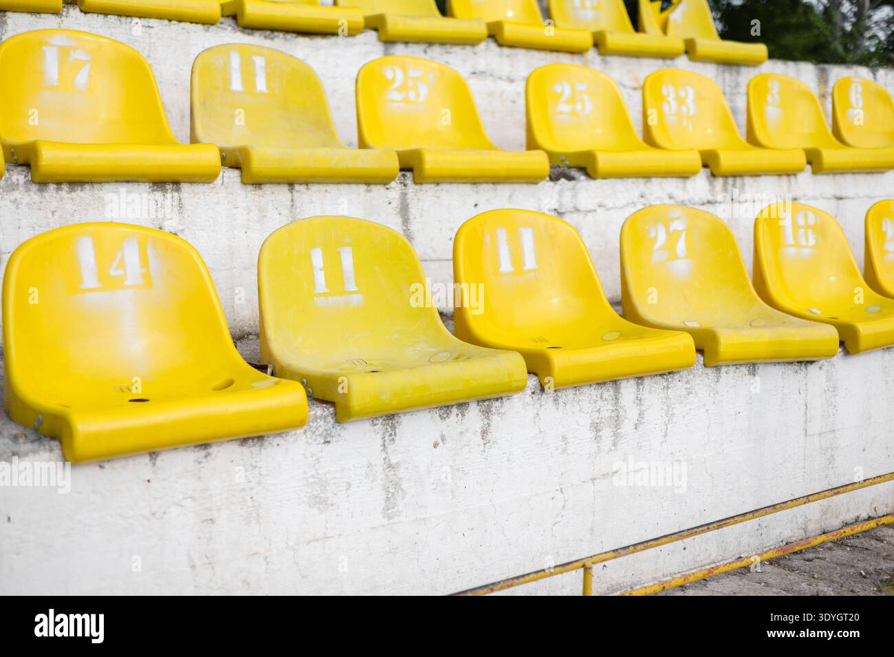 File di posti a sedere gialli con numeri dipinti di bianco su una tribuna in cemento. Primo piano di spettatori gialli numerati seduti in un vecchio ou Foto Stock