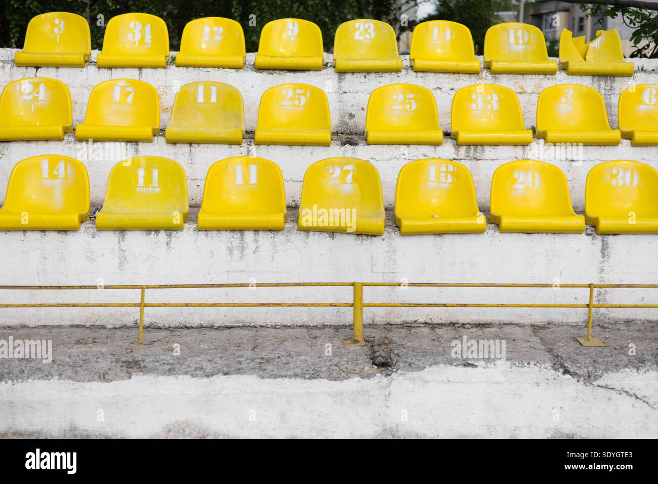 Vista frontale dei vecchi sedili in plastica gialli sui tribunali degli stadi in cemento intemprato. Palazzina sportiva abbandonata o in vecchio stile con sedie gialle e Foto Stock
