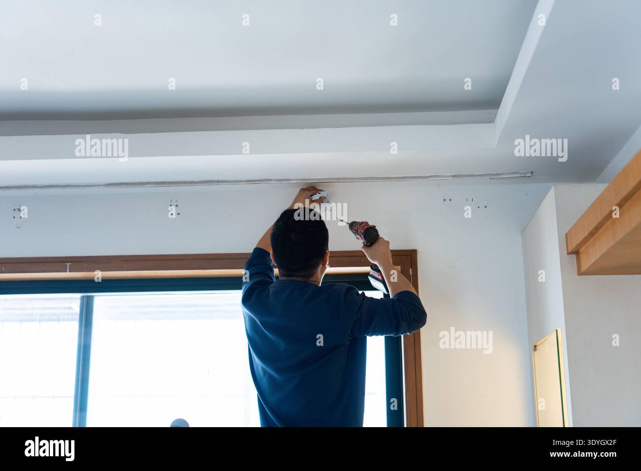 Uomo che installa lampada da soffitto in interni di casa moderna, vista da dietro, residenziale urbano Foto Stock