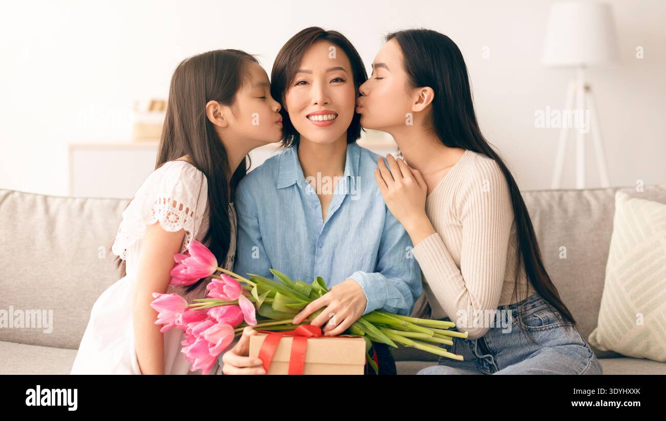 La madre riceve un regalo e fiori dalle sue figlie in un accogliente salotto Foto Stock