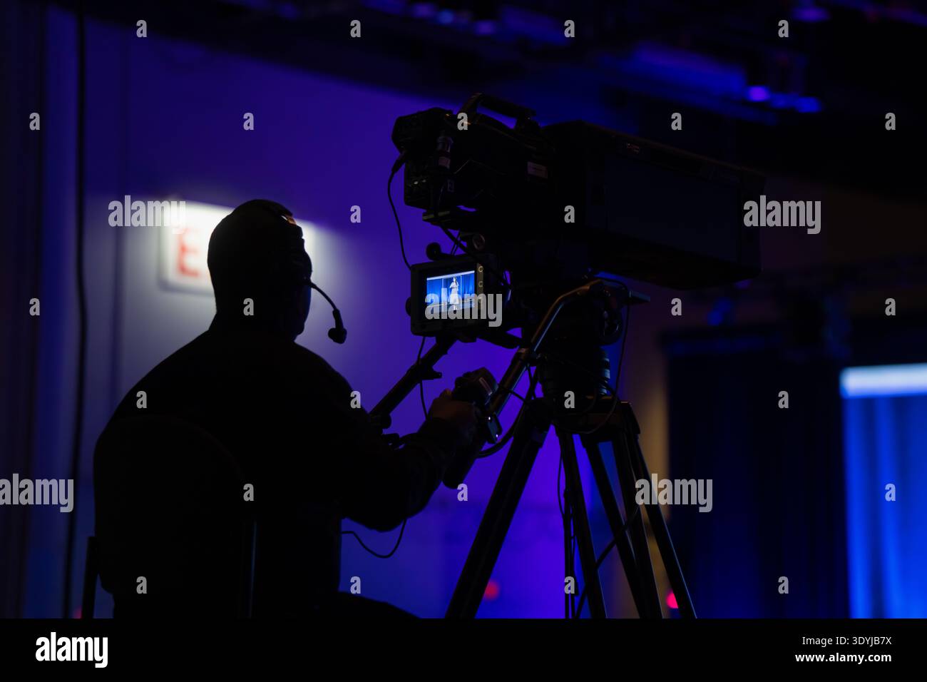 Sagoma di un operatore di telecamere di trasmissione che monitora un'esibizione dal vivo su un sistema video professionale durante un evento mediatico aziendale con luce blu Foto Stock