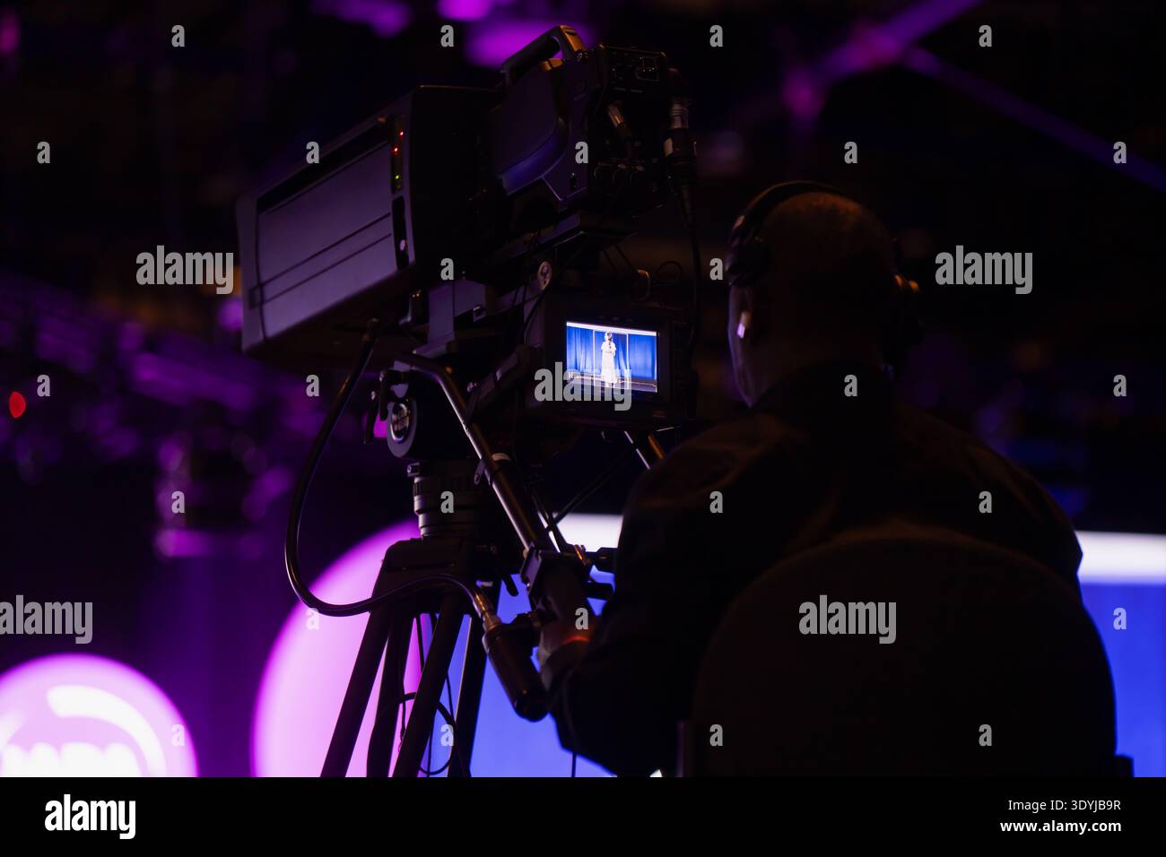 Un operatore video professionista che monitora il palco dal vivo attraverso un mirino digitale mentre filma una produzione televisiva in un teatro buio Foto Stock