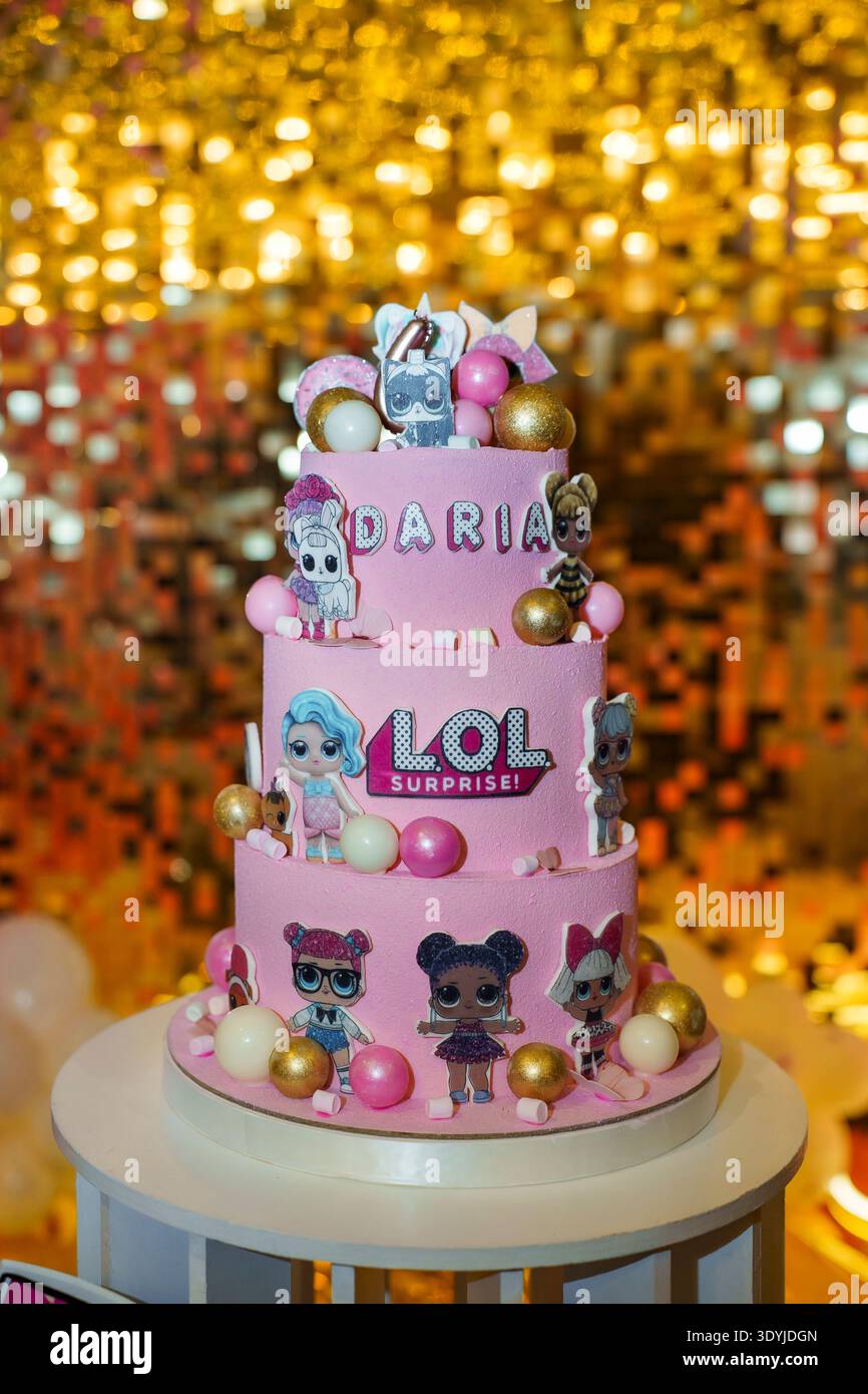Torta di compleanno rosa a tre livelli con bambole e topper personalizzato su sfondo dorato con paillettes Foto Stock