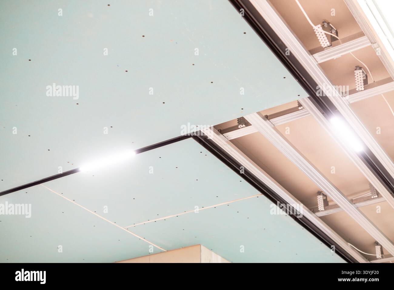 Primo piano dell'installazione a controsoffitto che mostra le strisce luminose a LED e le guide di montaggio in alluminio in un ambiente moderno. Foto Stock