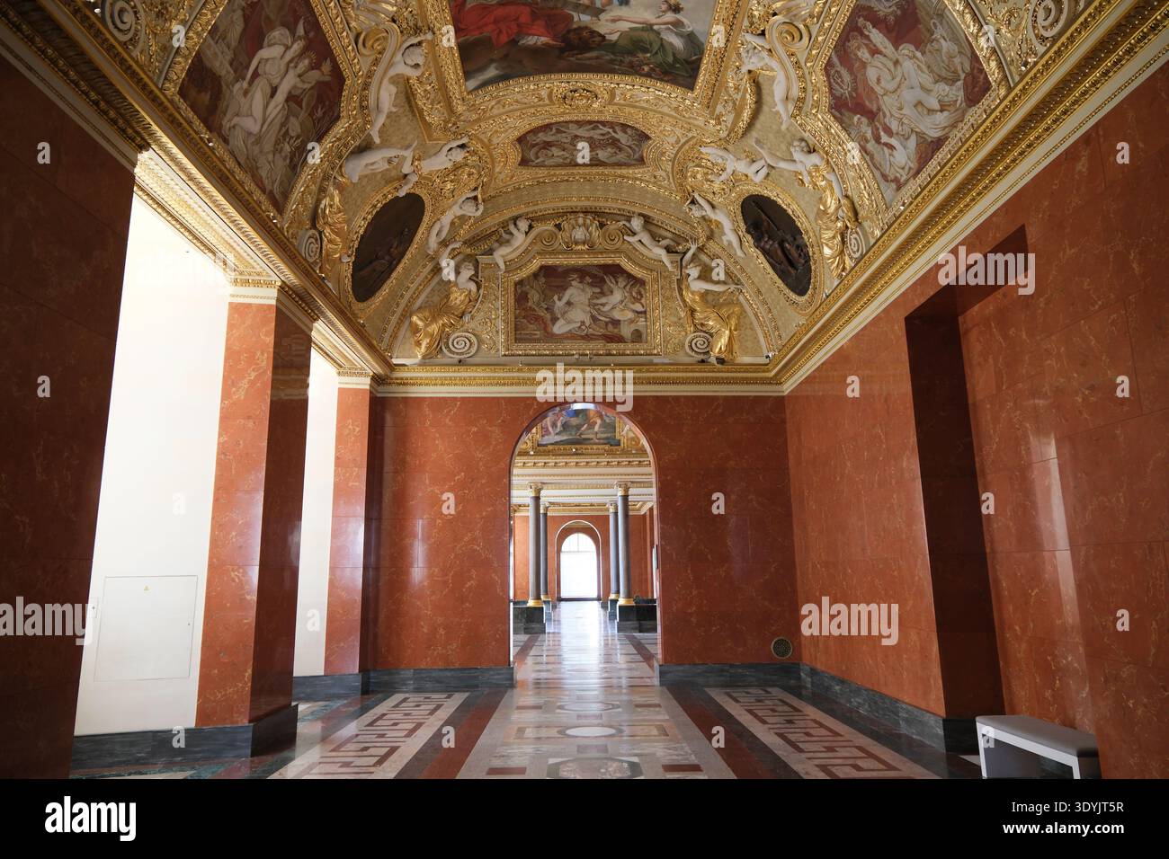 Parigi, Francia - 4 ottobre 2025: Prospettiva simmetrica di un grande corridoio con pareti in marmo rosso e soffitti decorati dorati affreschi all'interno del Museo del Louvre Foto Stock