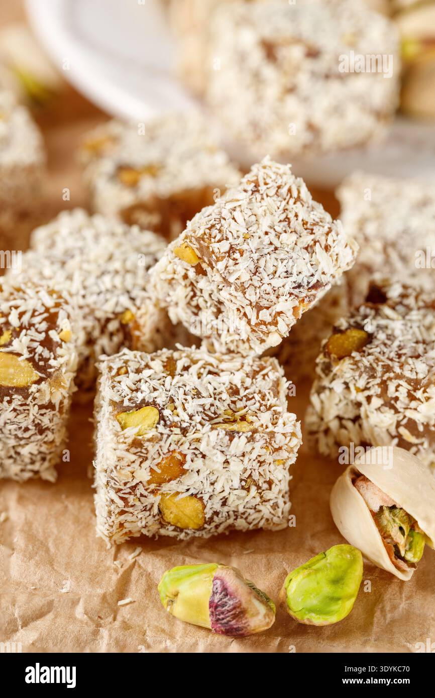Cubetti di delizia turca con noci di pistacchio e patatine di cocco primo piano su sfondo di carta. Dolci orientali tradizionali lokum Foto Stock