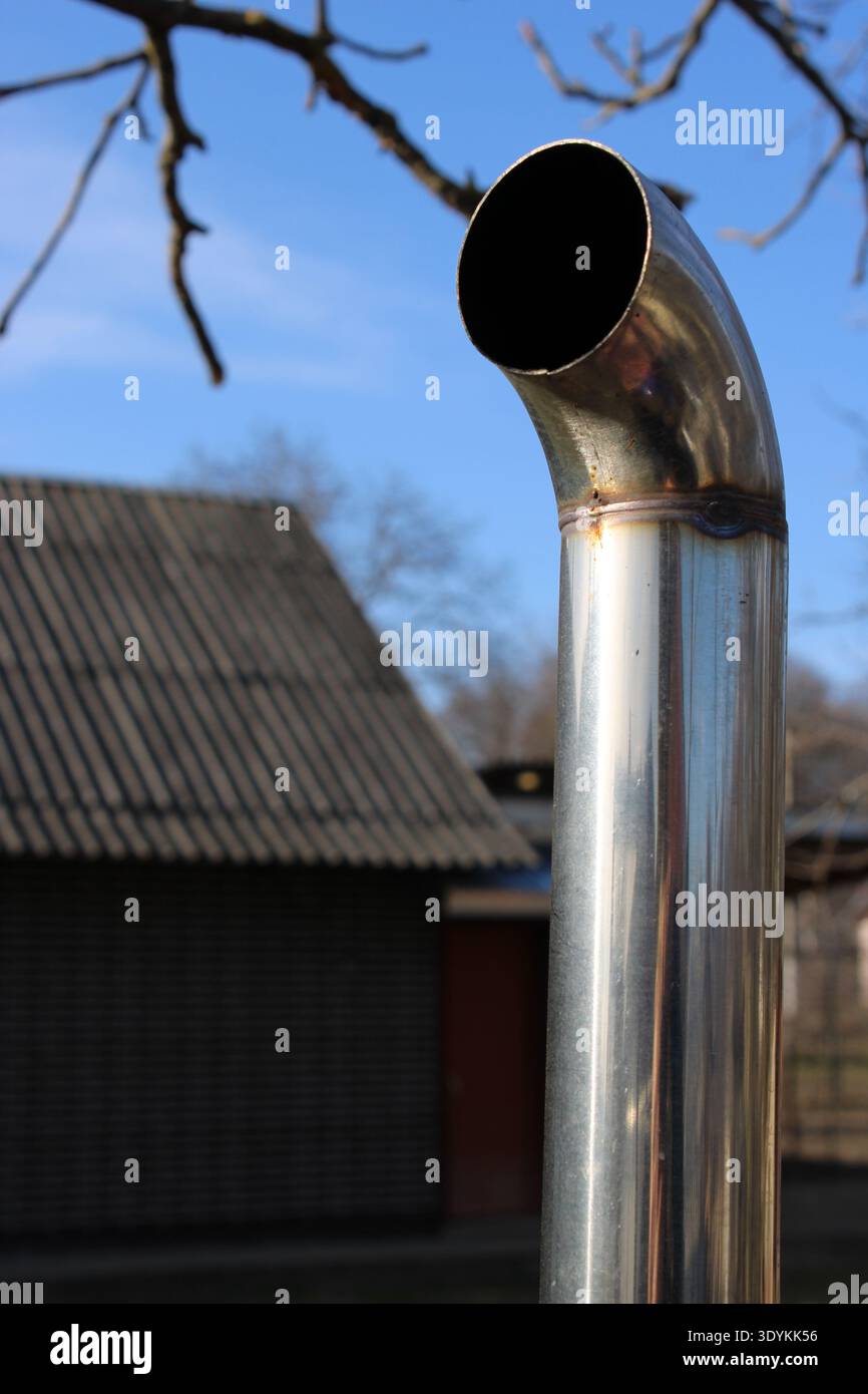 Un tubo di metallo lucido curva verso l'alto accanto ad un edificio in legno. Il cielo è limpido e blu. La scena cattura un momento all'aperto senza nessuno aro Foto Stock