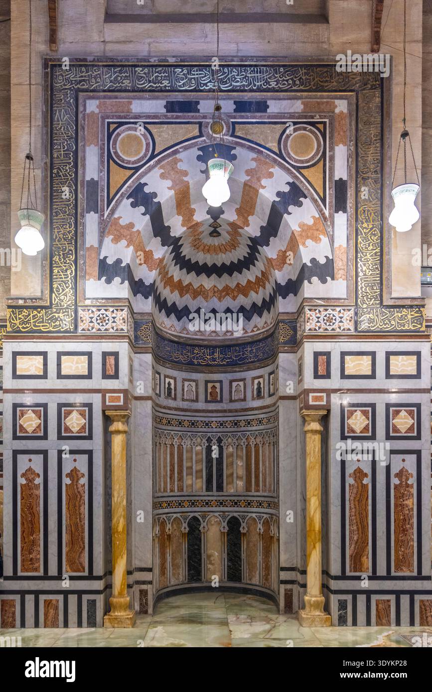 Elaborato mihrab islamico e interni decorati della moschea con intarsi in marmo, calligrafia araba e lampade a sospensione nella storica città del Cairo, in Egitto, showcasi Foto Stock
