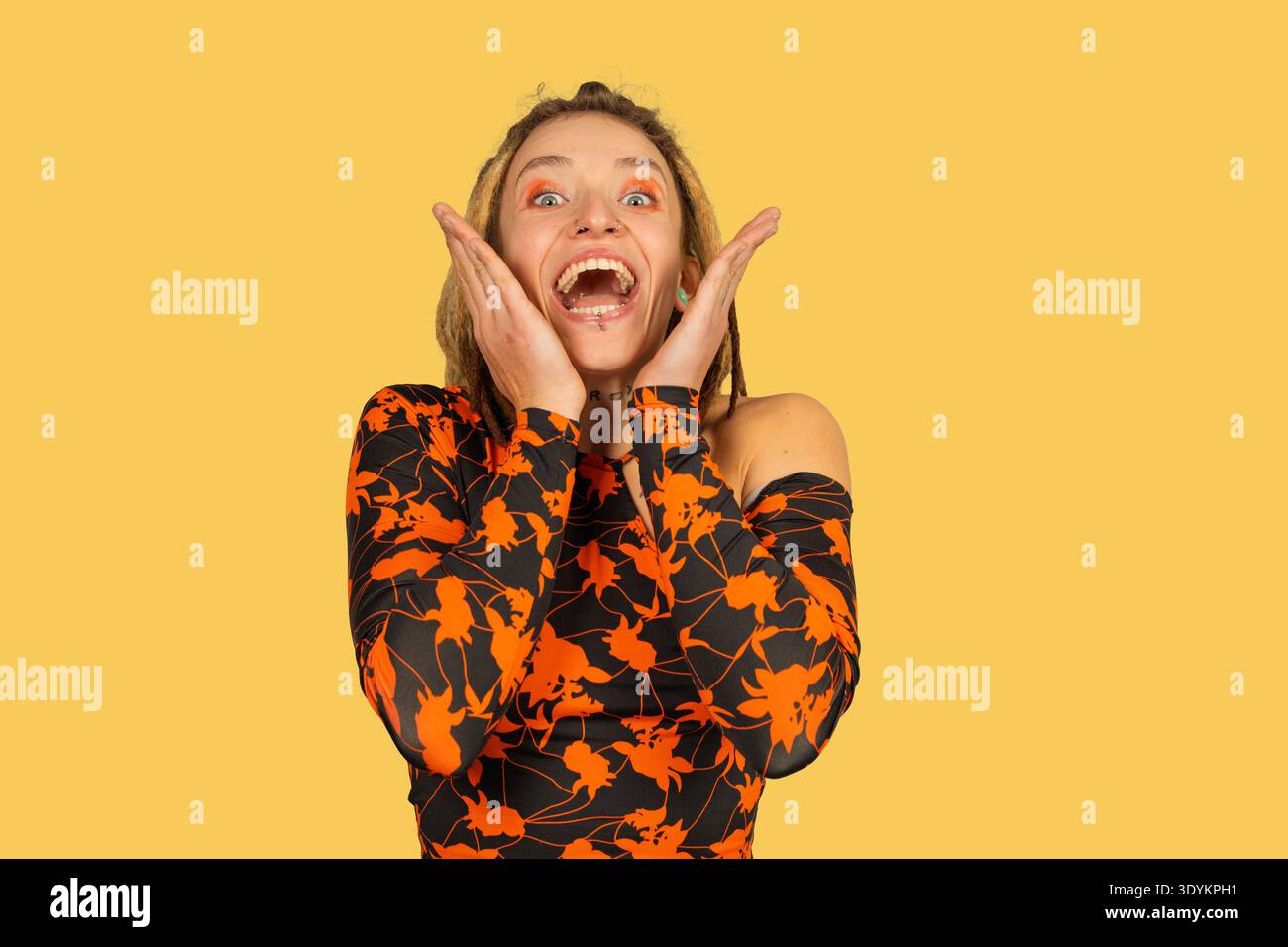 Donna che esprime sorpresa e gioia con le mani che inquadra il volto su uno sfondo giallo Foto Stock