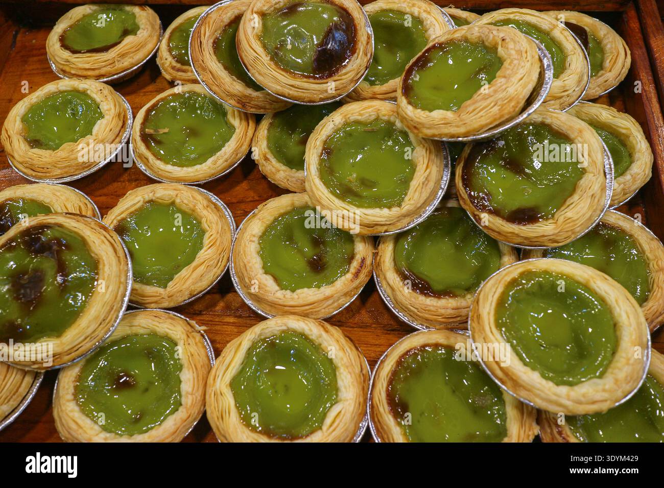 Crostate di uova di Matcha piene di crosta friabile e crema di tè verde che mostrano un moderno dessert fusion e un colorato concetto di Street food. Foto Stock