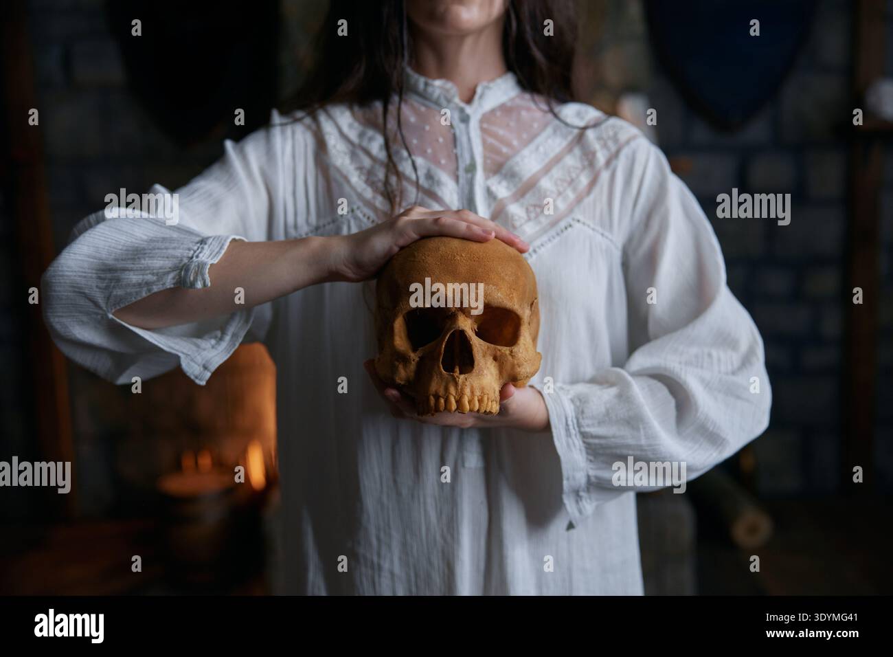 Donna che afferra delicatamente il cranio in mezzo a una pietra a lume di candela per uno studio contemplativo Foto Stock