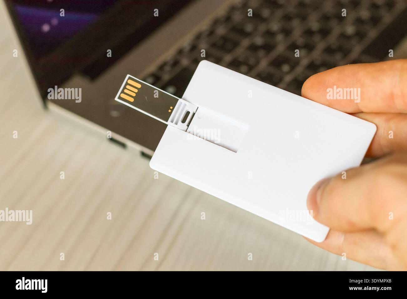 Una sottile scheda di memoria USB bianca inserita nello slot USB laterale di un computer laptop su un tavolo di legno chiaro. Foto Stock