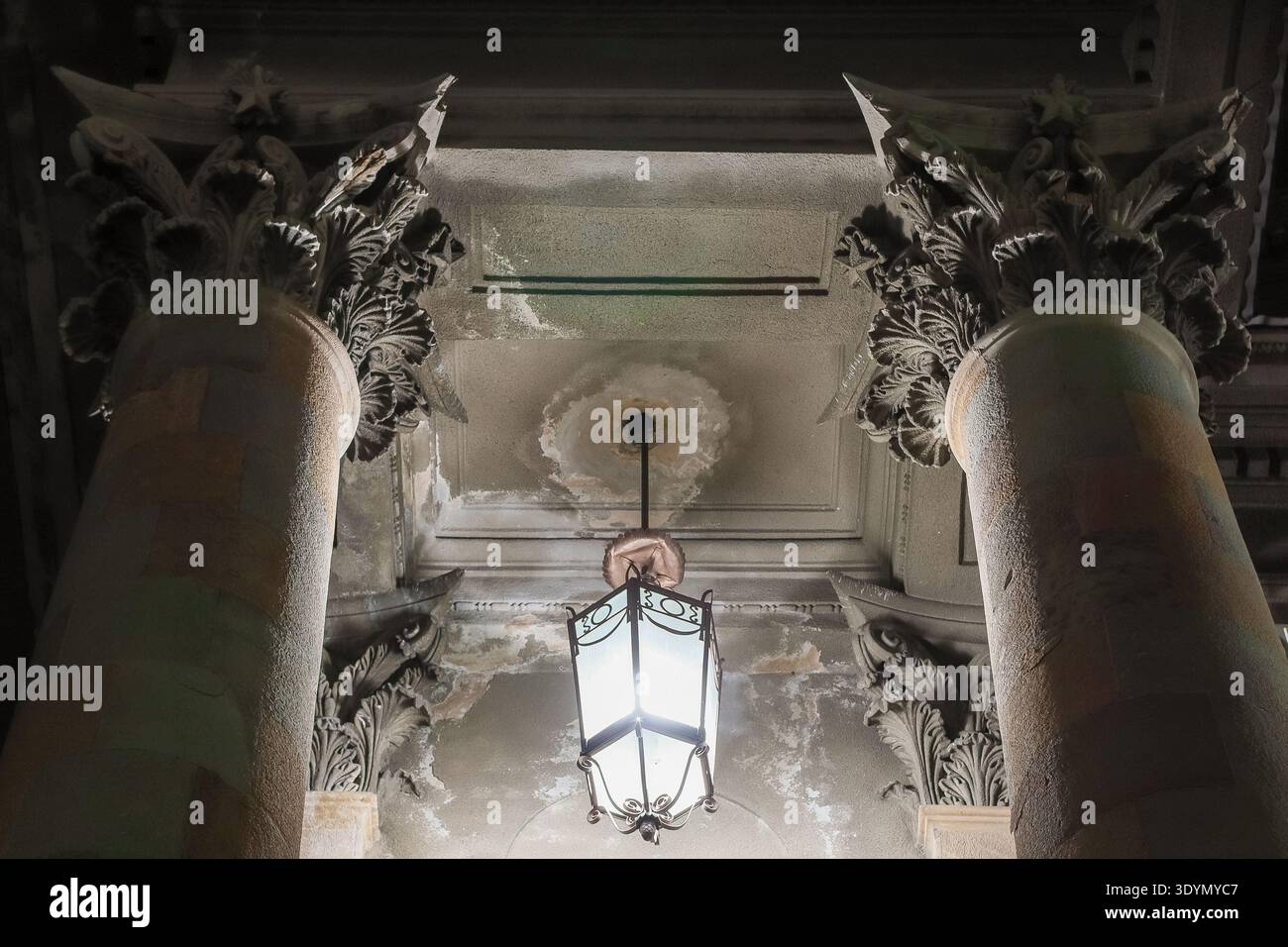 Vista dettagliata dei capitelli corinzi ornati e lanterna appesa sul soffitto antico con vernice sbucciante negli interni classici Foto Stock