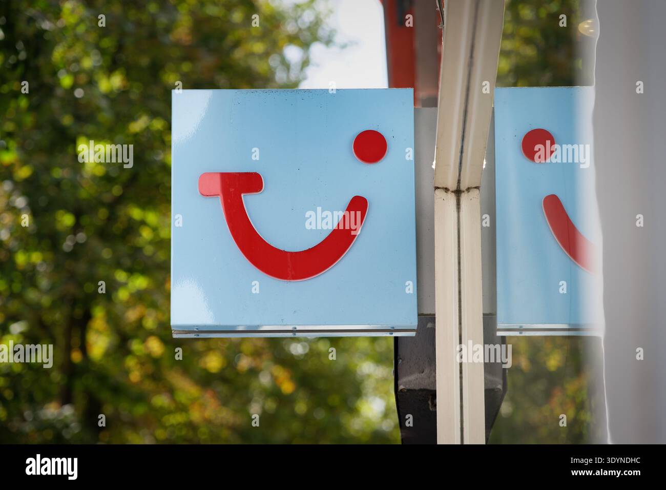 Colonia, Germania 15 agosto 2024: Primo piano dell'iconico logo rosso sorridente TUI su un cartello quadrato azzurro fuori dall'ufficio di un'agenzia di viaggi, con riflessi Foto Stock