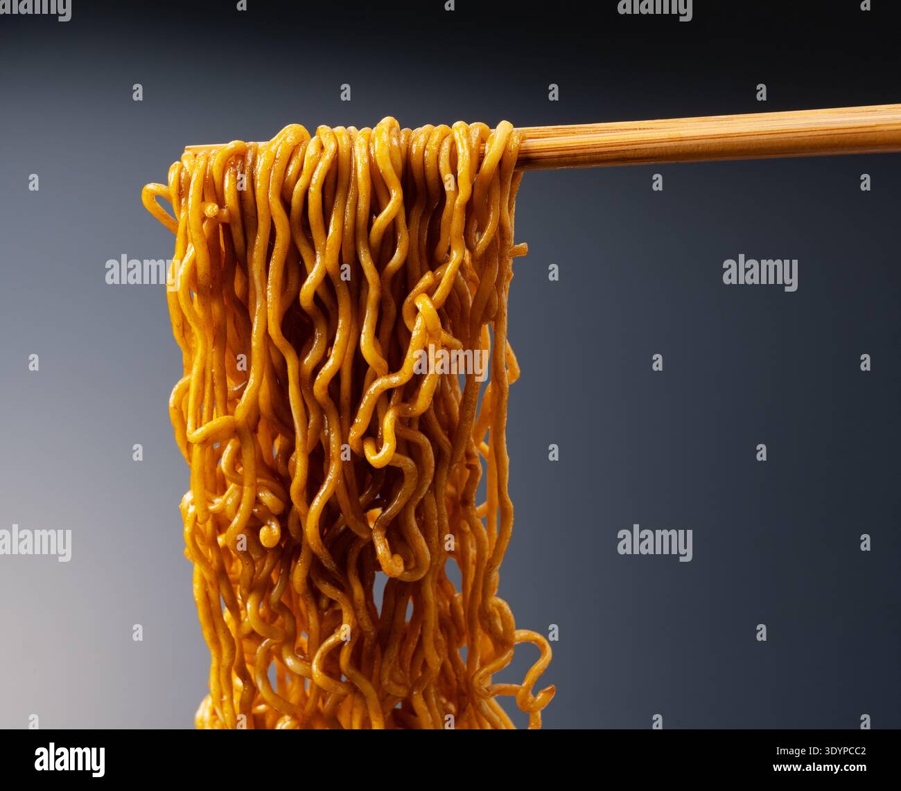Primo piano di noodle yakisoba istantanee lucide sollevate da bacchette di legno su uno sfondo scuro Foto Stock