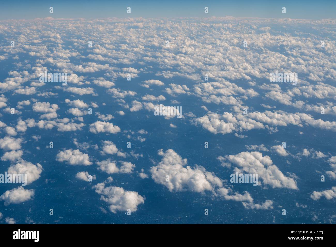 Guardando verso il basso su soffici nuvole nel cielo blu dalla finestra dell'aereo. Foto Stock